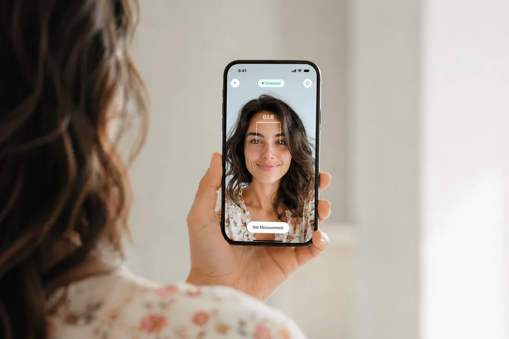 A woman holding an iPhone at arm's length while a PD app on the screen measures the distance between her pupils